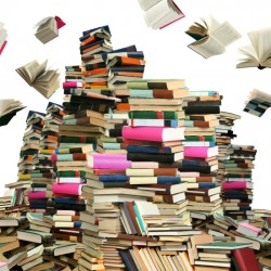 Huge stacks of colorful books piled high with some books flying open in the air above them.