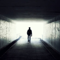 Silhouette of a person walking towards bright light at the end of a dark tunnel.