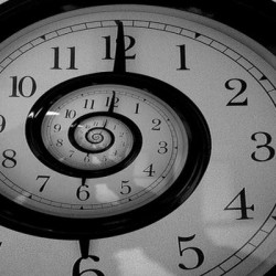 A black and white image of a clock face with a spiral effect distorting the numbers and hands.