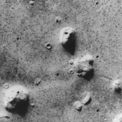 A black and white aerial image showing a rough, cratered surface with several raised mounds or small hills.