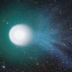 A bright comet with a glowing white nucleus and a blue-green tail streaks across a starry night sky.