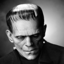 Black and white close-up portrait of Frankenstein's monster with prominent forehead bolts and textured skin.