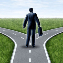 A man in a suit holding a briefcase standing at a fork in the road, facing two diverging paths.