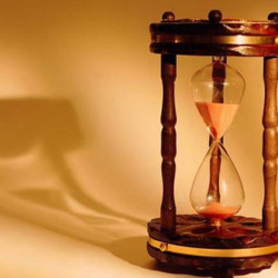 A wooden hourglass with sand flowing through, casting a shadow on a beige surface.
