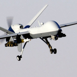 A white military drone equipped with missiles flying against a clear sky.