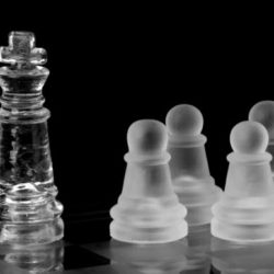 A clear glass king chess piece stands prominently against a black background with frosted pawns behind it.