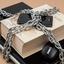 A book secured with metal chains and padlocks, along with a computer mouse and USB drive, symbolizing digital rights or information protection.