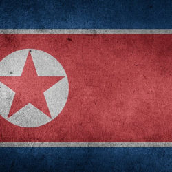 North Korean flag with a red star inside a white circle on a red background, bordered by blue and white stripes.