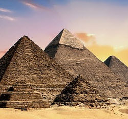 The iconic pyramids of Egypt stand majestically under a colorful sky at sunset in the desert.