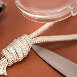 A close-up of a rope tied in a detailed knot next to a knife on a brown surface.